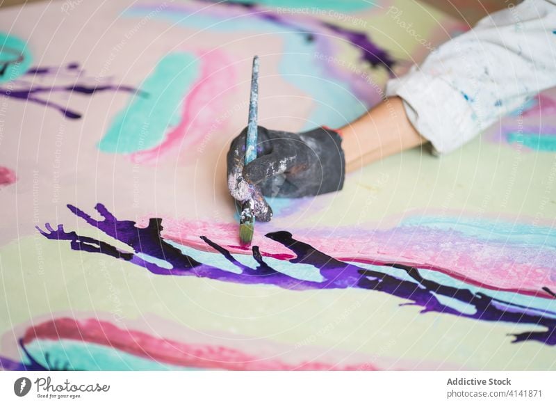 Crop unrecognizable artist with paintbrush mixing paints on palette talent craft process gouache workshop glove dirty plastic illustration studio robe woman