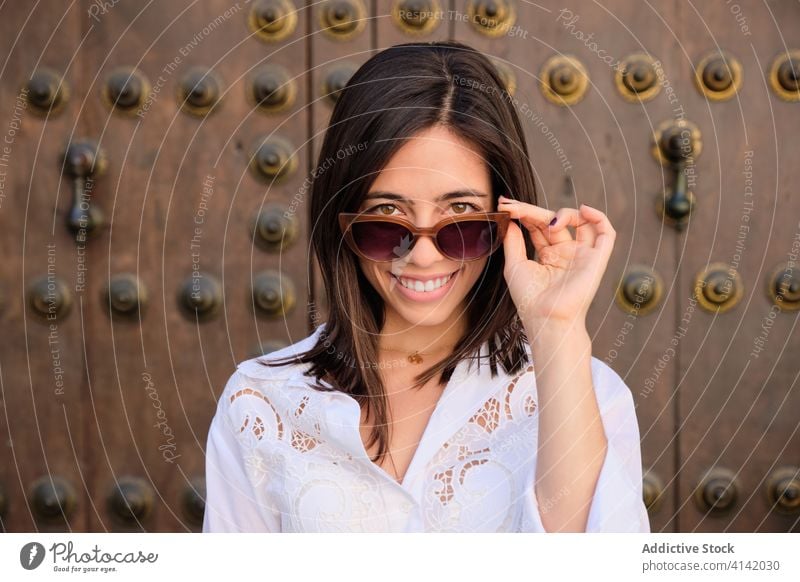 Charming woman smiling in city trendy style ancient fashion sunglasses gate ornament smile female street urban young positive happy cloth metal door historic