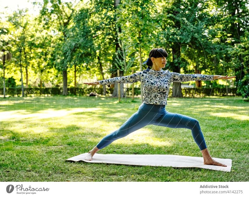 Content woman doing yoga in Virabhadrasana in park warrior pose practice flexible relax virabhadrasana mat barefoot female sportswear exercise healthy harmony