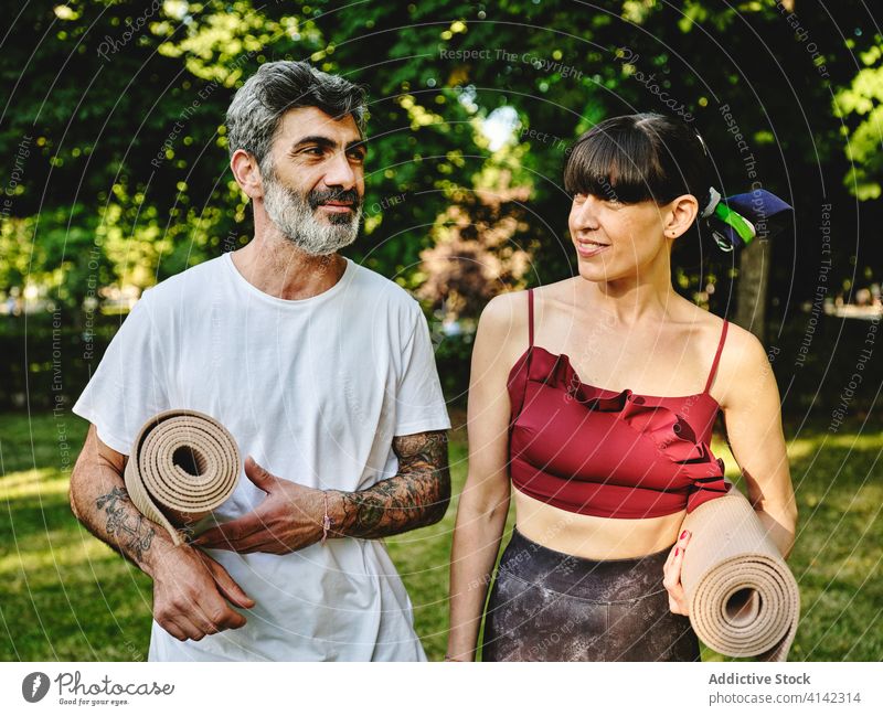 Cheerful couple with yoga mats walking in park cheerful together positive talk happy communicate conversation practice wellness activity nature content enjoy