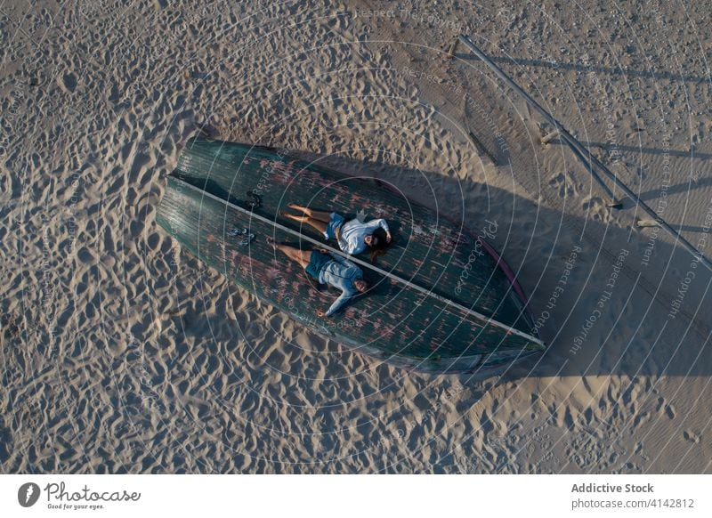 Relaxed couple resting on turned over rowboat on beach relax casual wooden upside down sand romantic coast relationship love carefree head on hands seaside