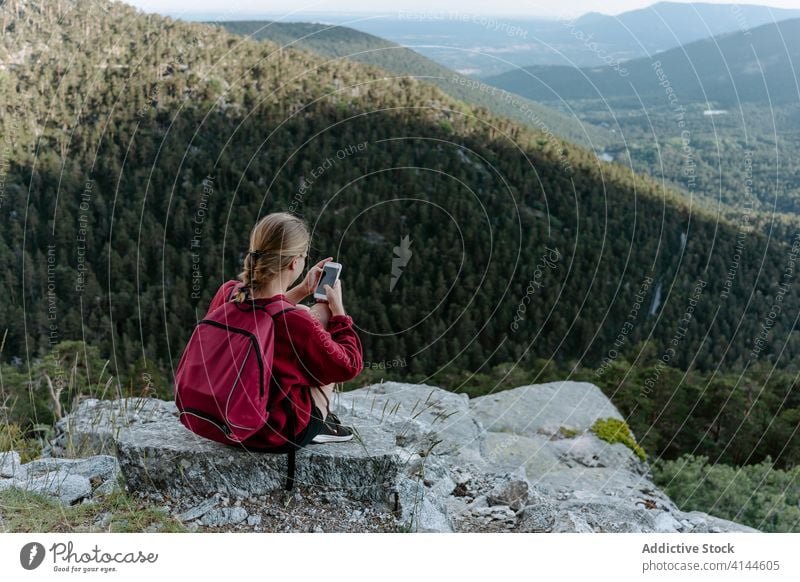 Female backpacker using smartphone while resting on mountain top woman hike travel activity trekking browsing check forest stone young nature adventure spain