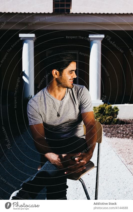 Happy man resting on chair in sunny inner yard toothy smile patio cheerful enjoy relax happy terrace positive comfort confident candid pose casual summer