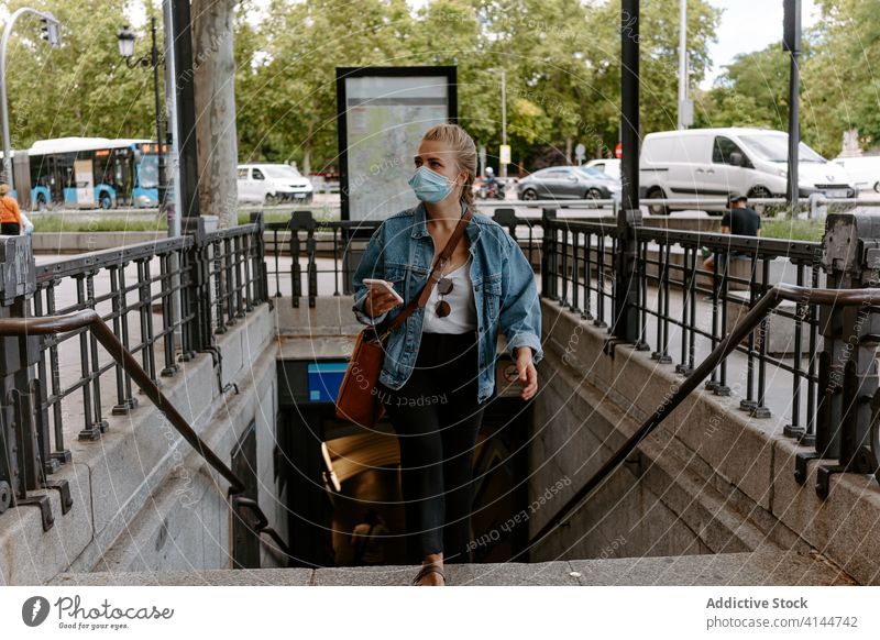 Young woman in mask with smartphone going upstairs on street city subway using urban coronavirus new normal lifestyle pandemic covid protect prevent covid19