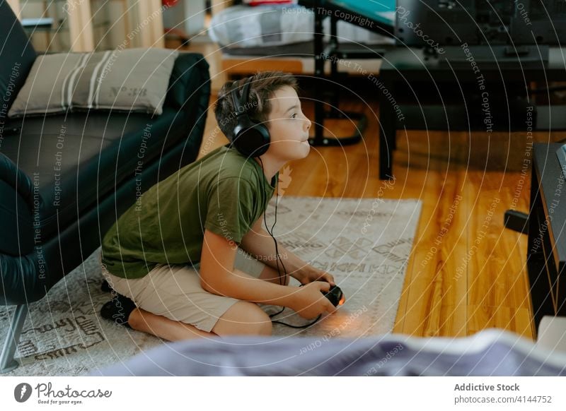 Focused child playing video game on couch boy joystick sofa legs crossed home entertain device gadget leisure concentrate kid little casual relax focus comfort