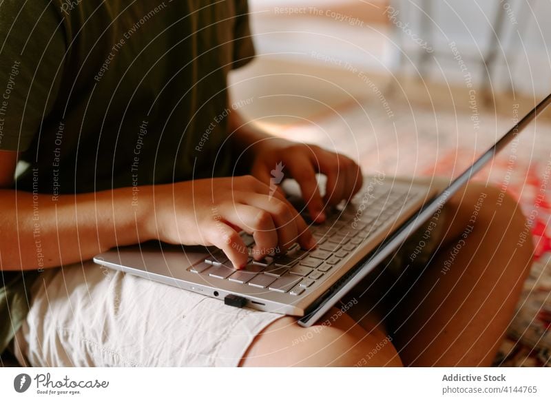 Focused kid using laptop at home boy typing floor internet legs crossed device gadget browsing online connection child little casual childhood smart digital