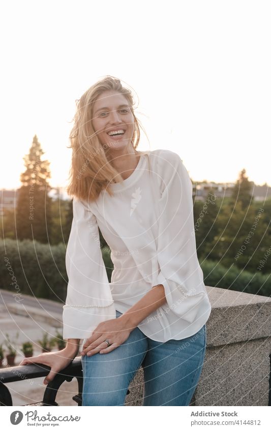 Joyful woman sitting on sidewalk railing and laughing joyful rest expressive cheerful toothy smile urban enjoy sunset delight relax happy madrid spain street