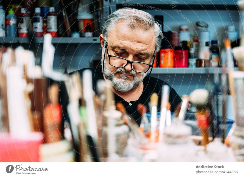 Male artist working behind set of various paintbrushes designer workplace studio collection small business sketch focus occupation profession watercolor painter