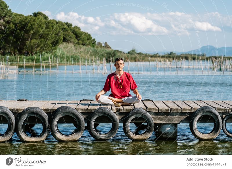 Calm male relaxing in Virasana pose during yoga session on pier man meditate virasana hero namaste peaceful sea calm harmony healthy tranquil nature wellness