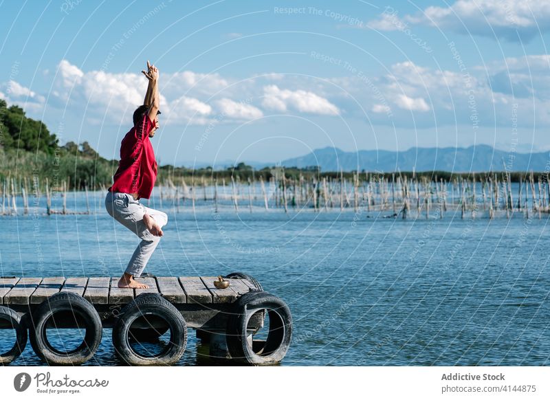 Focused man standing on sea embankment in Figure Four yoga pose practice figure four eka pada utkatasana quay morning harmony balance tranquil calm male casual