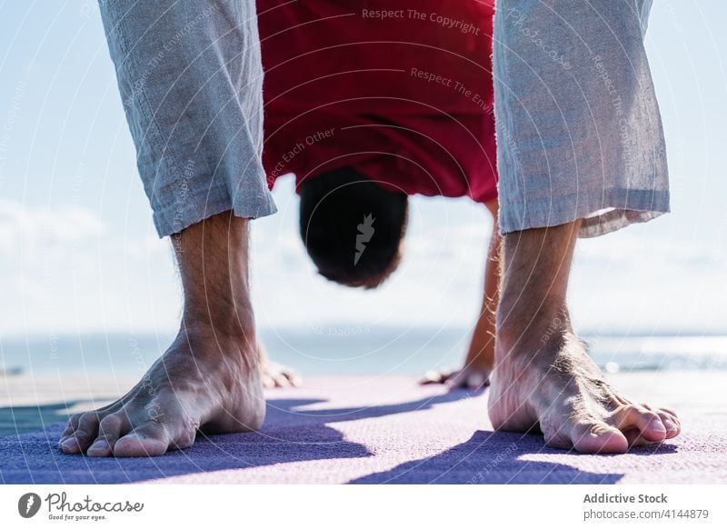 Barefooted man standing in Wheel asana while practicing yoga on seafront wheel urdhva dhanurasana upside down practice flexible healthy wellness harmony