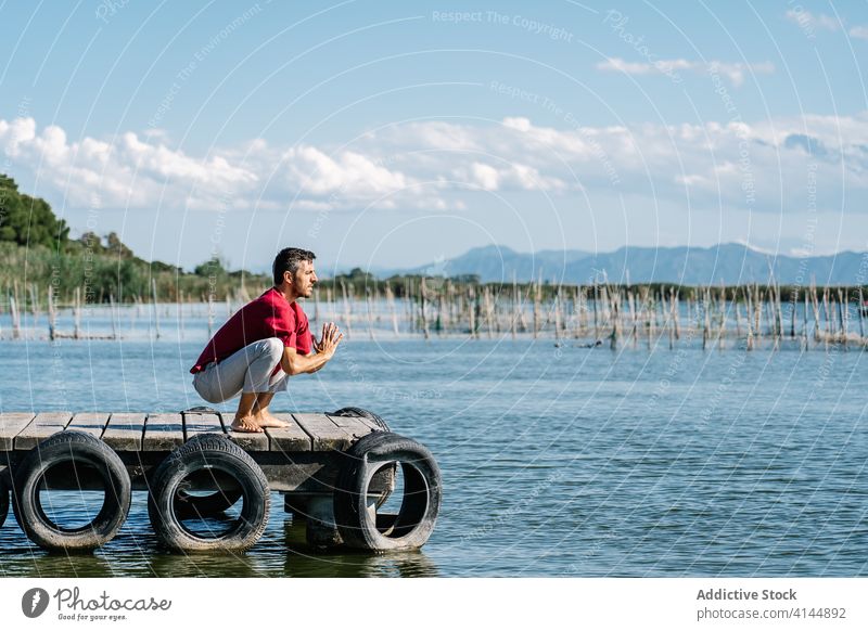 Focused man performing Malasana yoga position on embankment against sea garland malasana practice concentrate healthy harmony pier relax male casual stretch