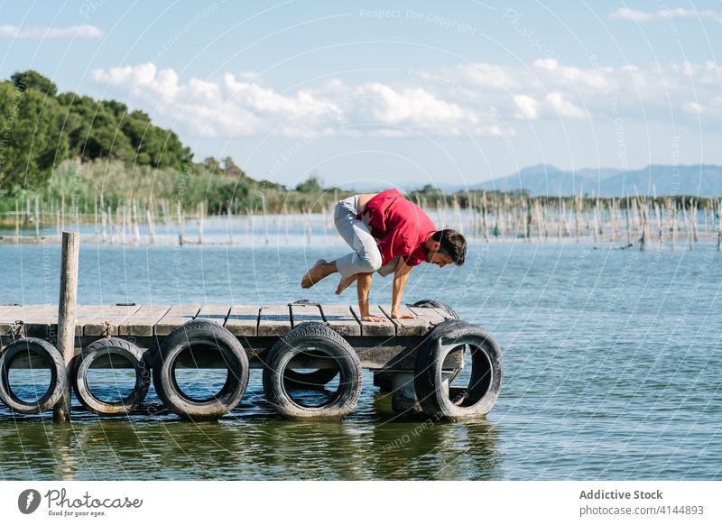 Concentrated man standing on arms in Crow position during yoga session on seafront crow kakasana balance strength quay practice healthy wellness stress relief