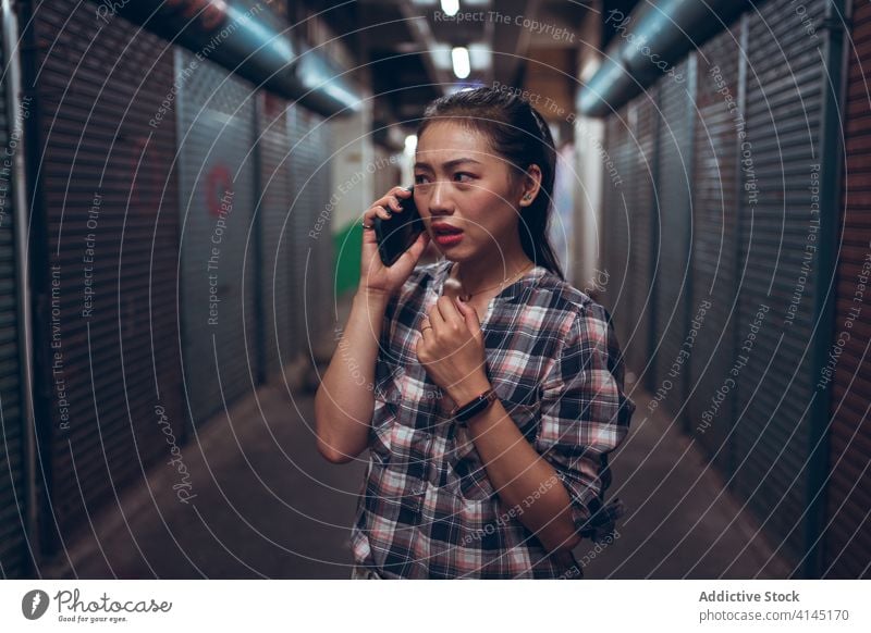 Worried young woman talking on smartphone in underground corridor call scare worried unhappy passage frown sad dark communicate speak connection conversation