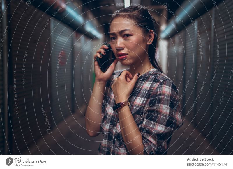 Worried young woman talking on smartphone in underground corridor call scare worried unhappy passage frown sad dark communicate speak connection conversation