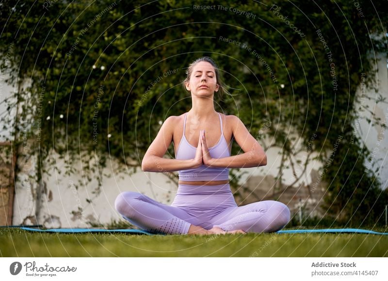 Woman meditating in Lotus pose in courtyard meditate yoga lotus pose woman peaceful asana padmasana namaste gesture tranquil female active wear calm zen relax