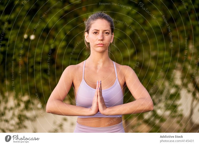 Calm woman practicing yoga with namaste hands gesture calm tranquil mat female backyard courtyard bra leggings slim wellness asana practice harmony healthy lady