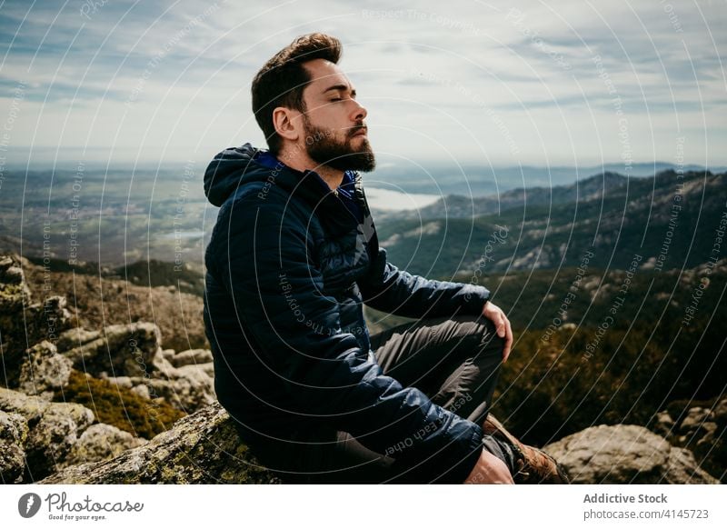 Bearded man meditating in mountains meditate traveler rest eyes closed legs crossed nature puerto de la morcuera spain male sky cloudy rock sit stone yoga