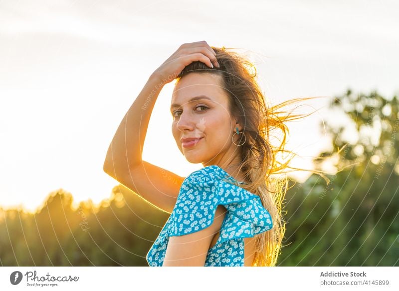 Happy young woman relaxing near green trees in countryside touch hair romantic wind sunset enjoy happy traveler smile cheerful rest female style trendy