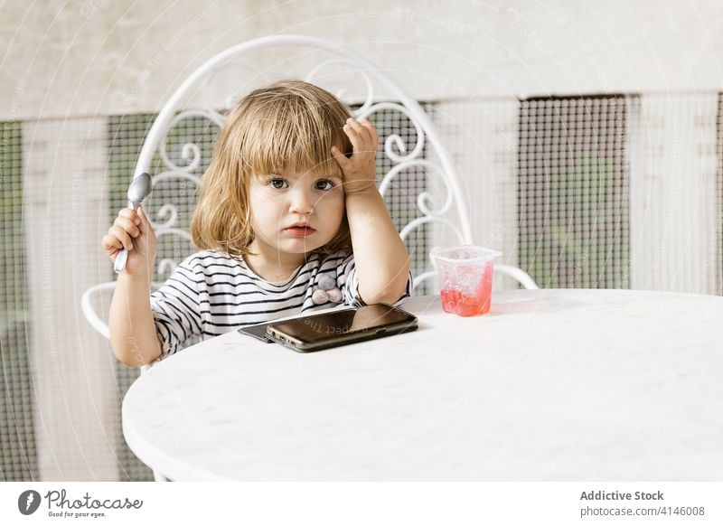 Kid eating jelly and using smartphone on terrace child watch cartoon little girl entertain summer backyard table cute childhood sit kid rest adorable relax