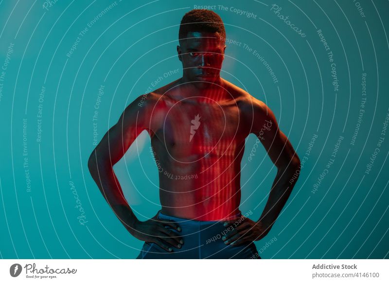 Shirtless athlete standing in colorful studio sportsman runner shirtless muscular determine confident active physical neon young black african american ethnic