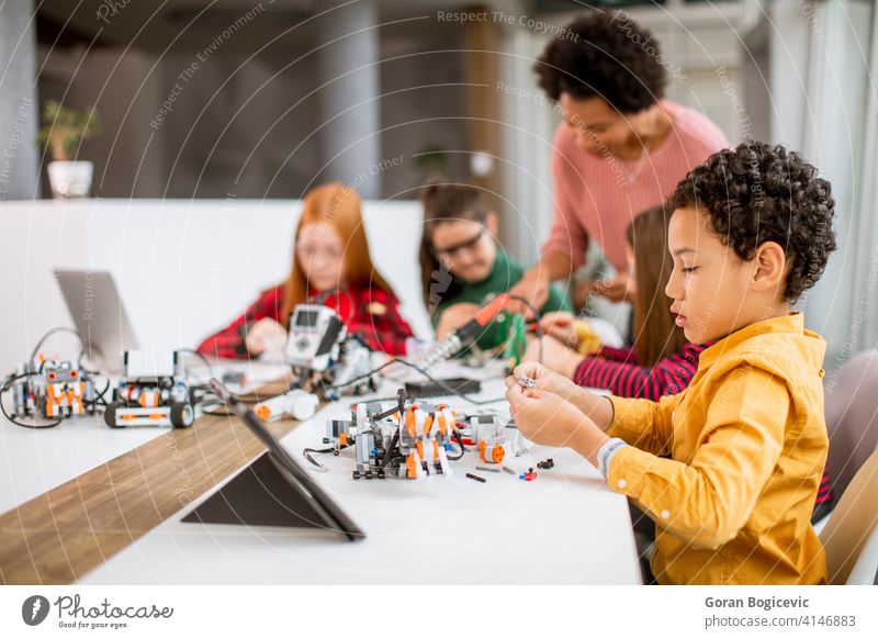 Happy kids with their African American female science teacher with laptop programming electric toys and robots at robotics classroom education technology