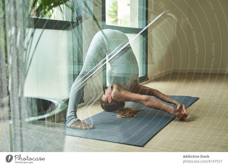 Strong sportswoman doing difficult variation of Wide Legged Forward Bend yoga pose strength body prasarita padottanasana c studio practice concentrate