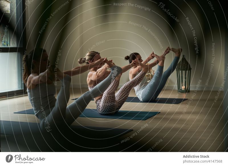 Fit sportswomen doing stretching and balancing asana during yoga session practice balance boat with double toe hold lesson studio wellness healthy exercise