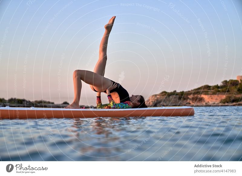 Flexible woman doing yoga on paddleboard sunset pose surfer balance sea female water healthy nature harmony relax tranquil serene sky calm ocean peaceful lady