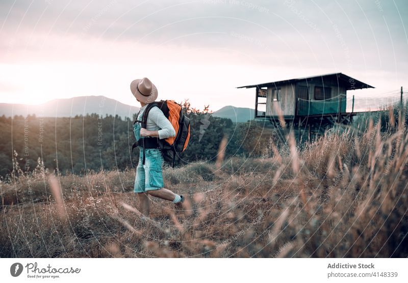 Anonymous man in rural area traveler sunset mountain enjoy field backpack tourist evening male picturesque sundown wanderlust sky tourism village happy