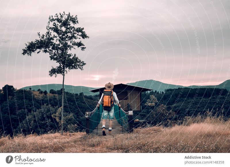 Anonymous traveling man walking along wooden footbridge suspension tourist backpack admire landscape vacation male adventure trip tourism content journey