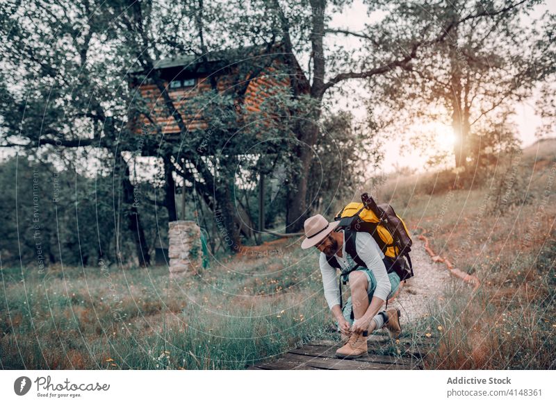 Male tourist with backpack tying shoelaces traveler forest man tie trekking path wooden backpacker nature male adventure hike explore trip tourism activity guy