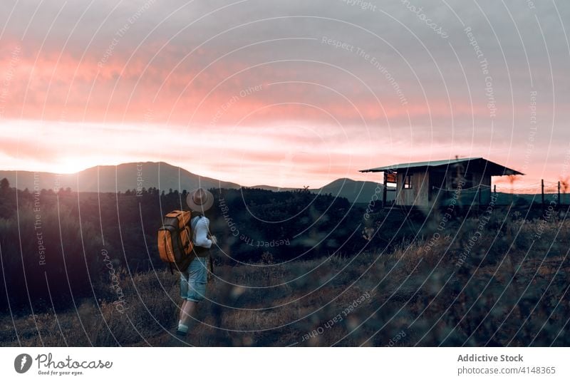 Anonymous man in rural area during sunset traveler mountain enjoy field backpack tourist evening male picturesque sundown wanderlust sky tourism village