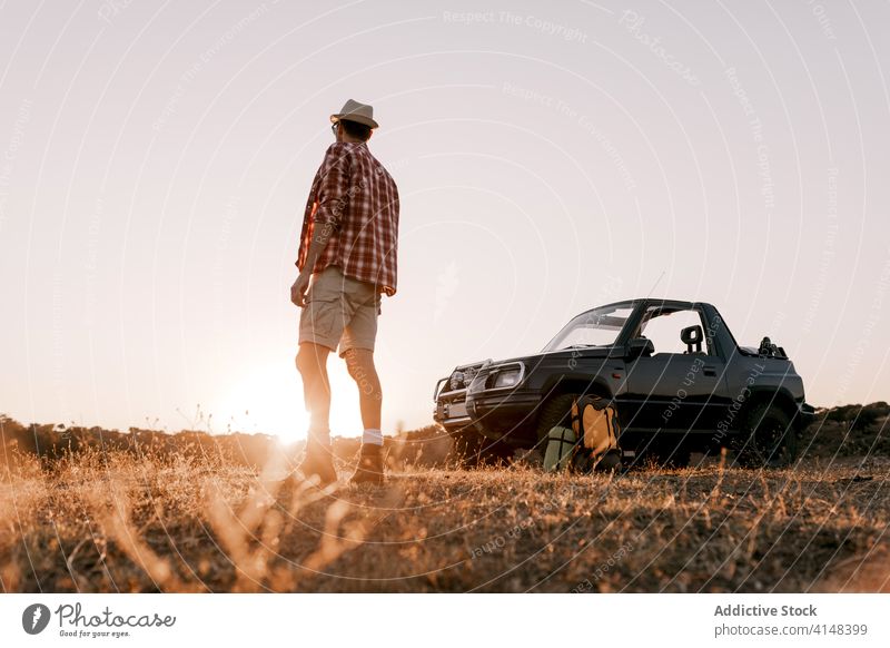 Unrecognizable male traveler admiring landscape near car in sunlight tourist admire nature grass trip vacation harmony sunshine beauty idyllic picturesque