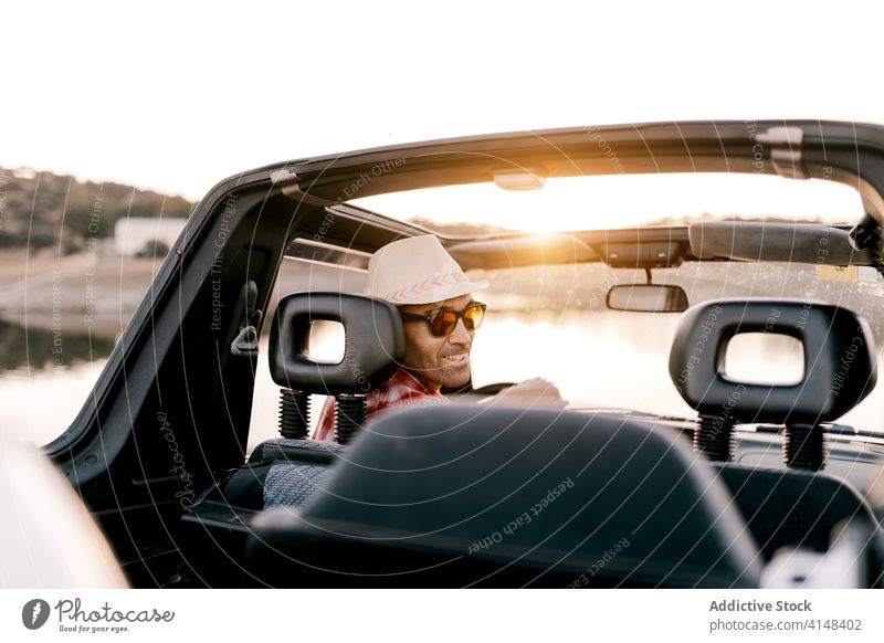 Smiling male traveler driving car near lake in sunshine tourist drive vacation mountain nature weekend content inside tourism harmony automobile trip highland