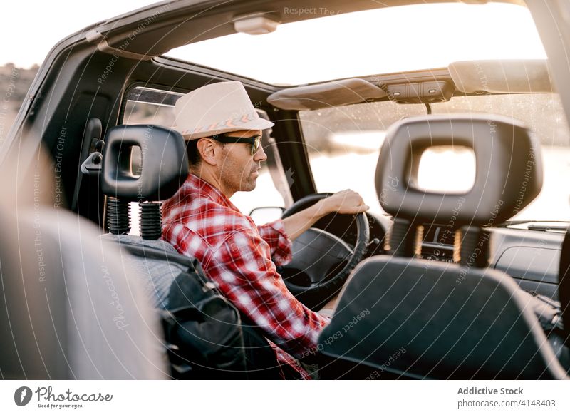 Smiling male traveler driving car near lake in sunshine tourist drive vacation mountain nature weekend content inside tourism harmony automobile trip highland