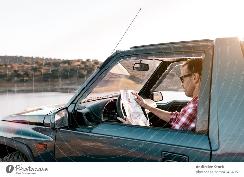 Unrecognizable tourist looking at map inside car parked near lake watch destination navigate route vacation river mountain tourism location weekend nature