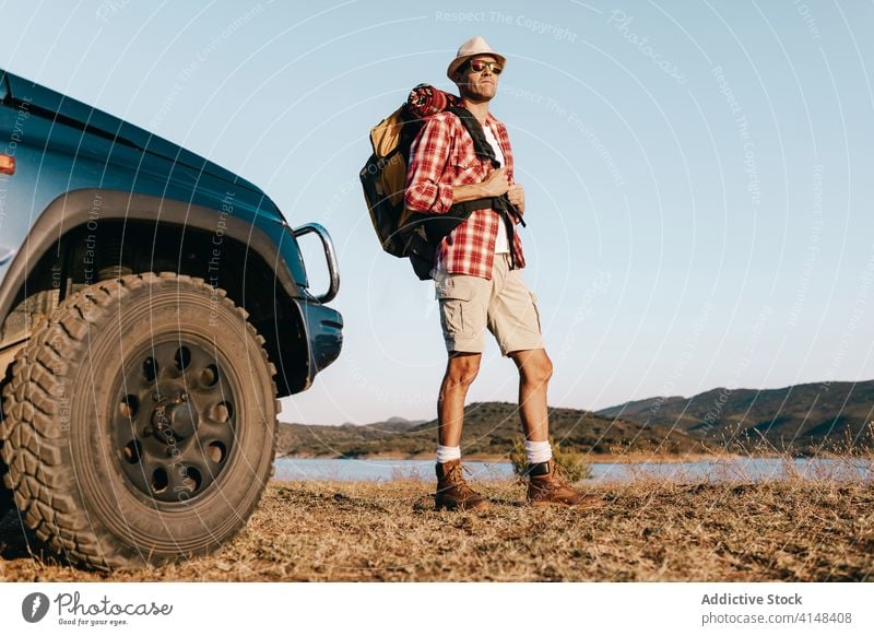 Male traveler admiring landscape near car in sunlight tourist admire nature grass trip vacation harmony sunshine beauty idyllic picturesque tourism man calm