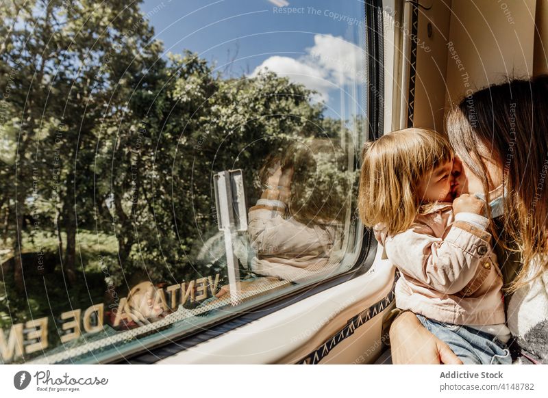 Content woman and child in train travel kiss mother coronavirus mask together playful entertain having fun girl kid joy childhood daughter parent sit motherhood