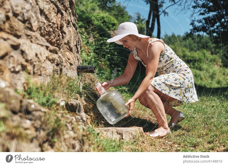 Woman with bottle of water in countryside natural spring woman aqua fill pour fresh refreshment female sunhat dress plastic nature beverage summer liquid