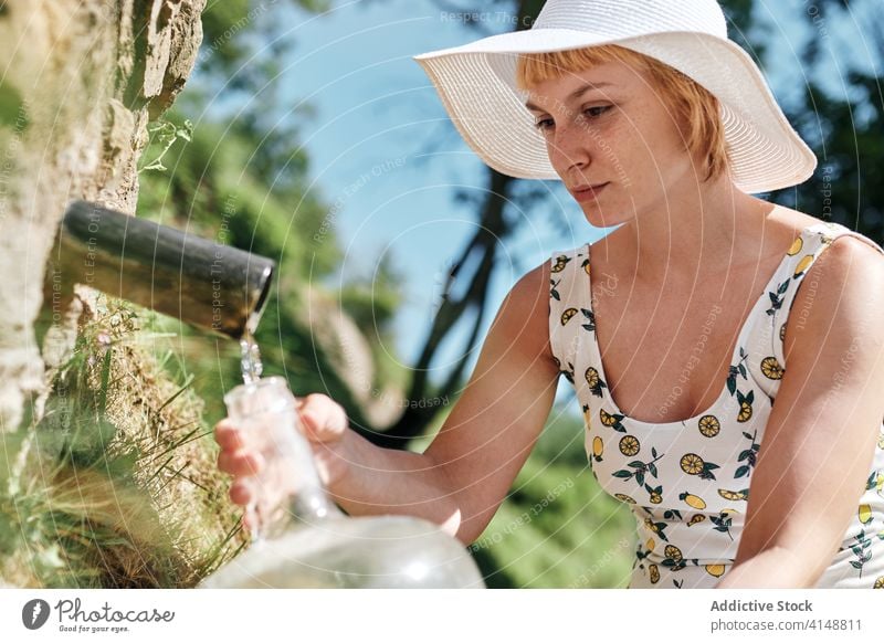 Woman with bottle of water in countryside natural spring woman aqua fill pour fresh refreshment female sunhat dress plastic nature beverage summer liquid