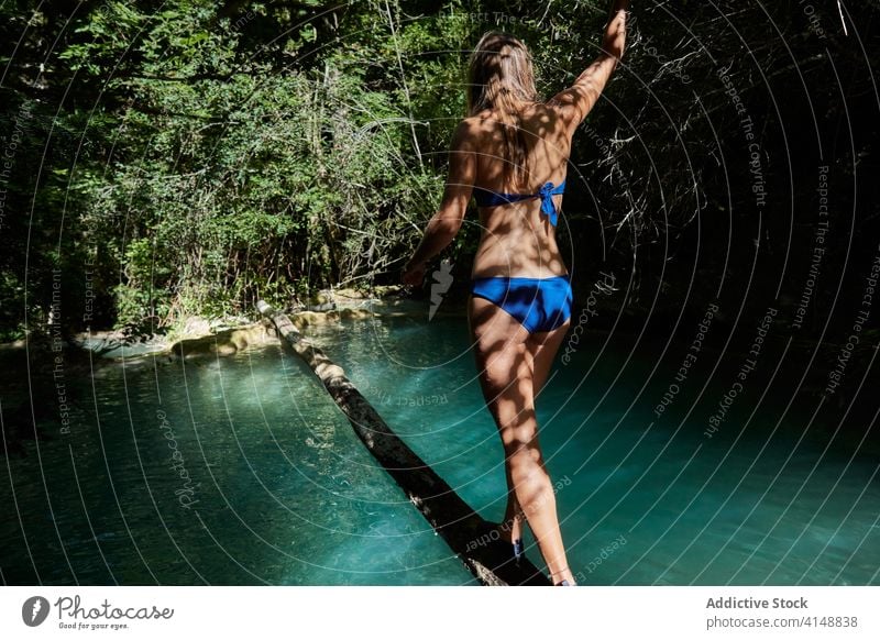 Young woman crossing lake in woods log trunk anonymous travel walk back view bikini young forest nature shore vacation adventure trip tourism wanderlust explore