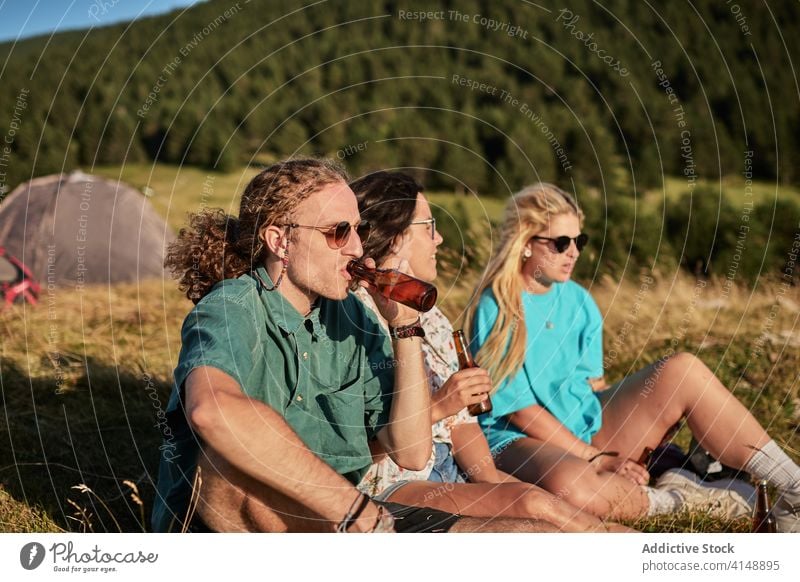 Relaxed travelers on hill in summer company relax drink beer together tent camp campsite sunny friendship rest nature vacation weekend beverage enjoy recreation