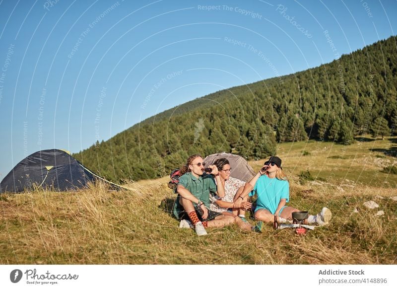 Relaxed travelers on hill in summer company relax drink beer together tent camp campsite sunny friendship rest nature vacation weekend beverage enjoy recreation