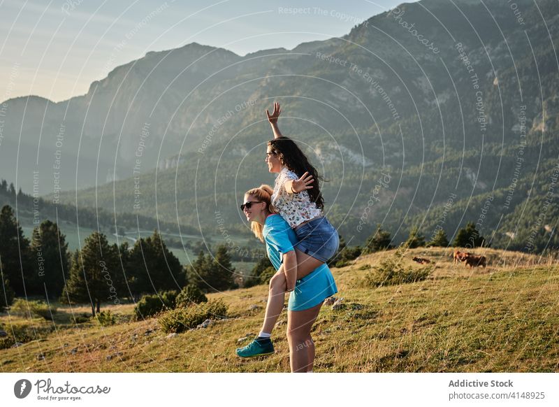 Happy women enjoying summer in mountains piggyback friend carefree having fun vacation playful majestic highland friendship landscape freedom friendly together