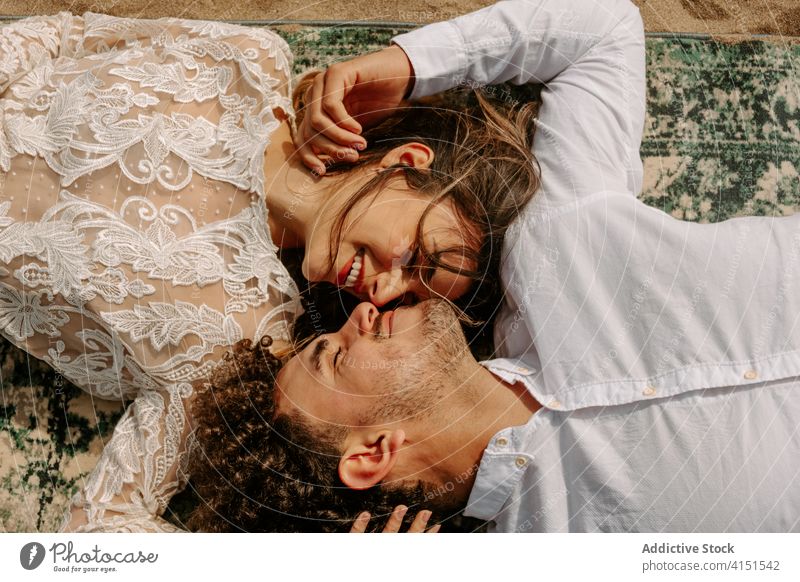 Affectionate couple cuddling on rug at the beach romantic newlywed together kiss embrace relationship sea love nature sand vintage passion cuddle gentle smile