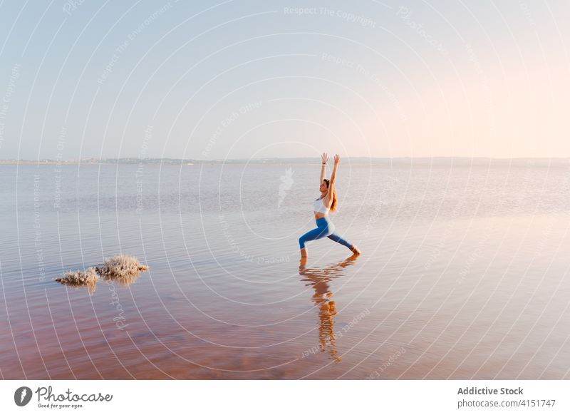 Woman practicing yoga asana in lake water woman practice pose stand warrior one Virabhadrasana evening balance calm focus harmony wellness bend serene