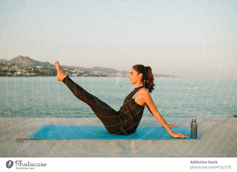 Woman practicing yoga in Boat asana woman boat pose navasana sea pier practice mat sunset female peaceful relax healthy sportswear healthy lifestyle