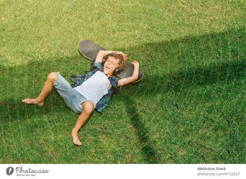 Child leaning on a skateboard while listening to music and singing on the grass teenager cool guy stylish youth dangerous enjoying extreme look kid trend