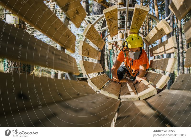 Kid in protective equipment entertaining in adventure park child safety mask covid 19 tunnel wooden crawl having fun harness coronavirus rope kid epidemic